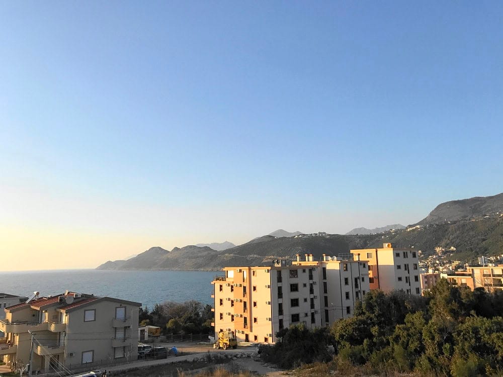 Panoramic sea and mountain view from an apartment in Dobra Voda, Montenegro: residential buildings and nature on a sunny day.