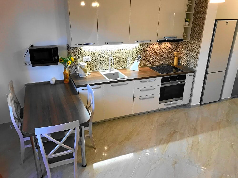 Modern kitchen in an apartment, Dobri Vody, Montenegro: white cabinetry, dining area, and mosaic backsplash.