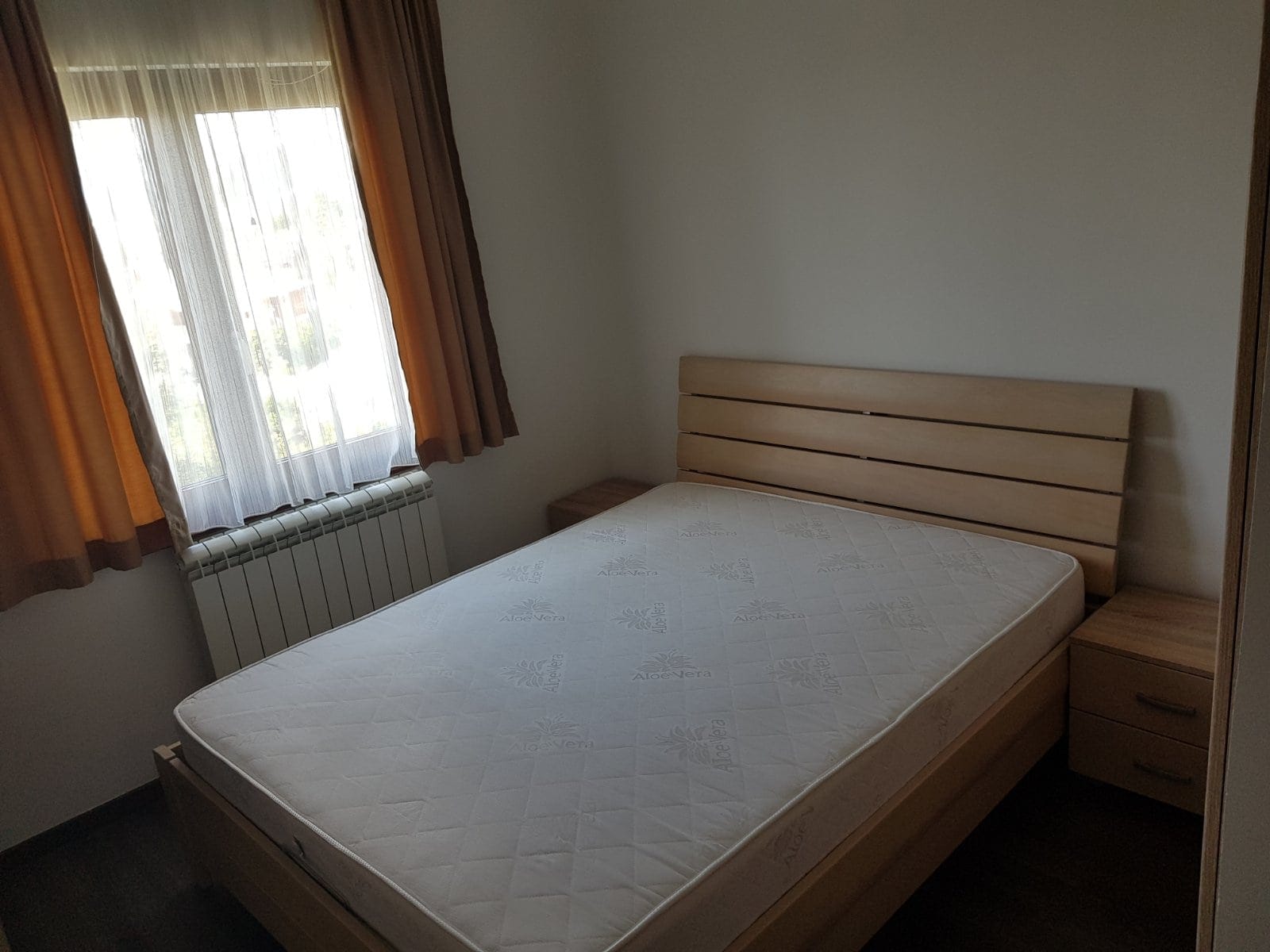 Svetla spavaća soba sa bračnim krevetom i noćnim ormarićima u kući na prodaju, grad Bar, Crna Gora.