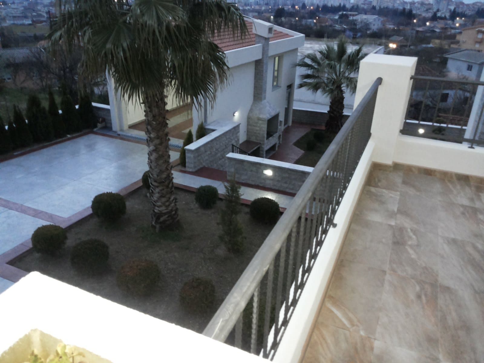 Pogled sa balkona na uređeno dvorište sa palmama i roštiljem kod privatne kuće u gradu Bar, Crna Gora.