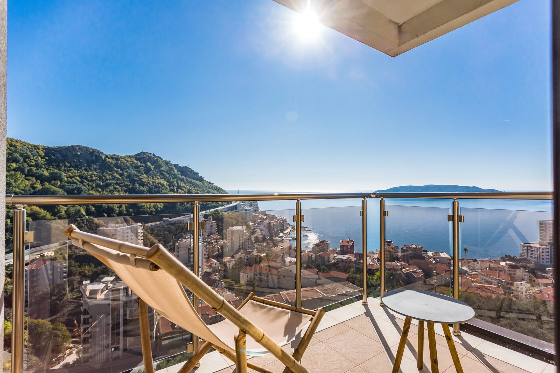 Balkon penthausa u Rafailovićima, Crna Gora: ležaljka, stočić i panoramski pogled na more, planine i budvansku obalu.