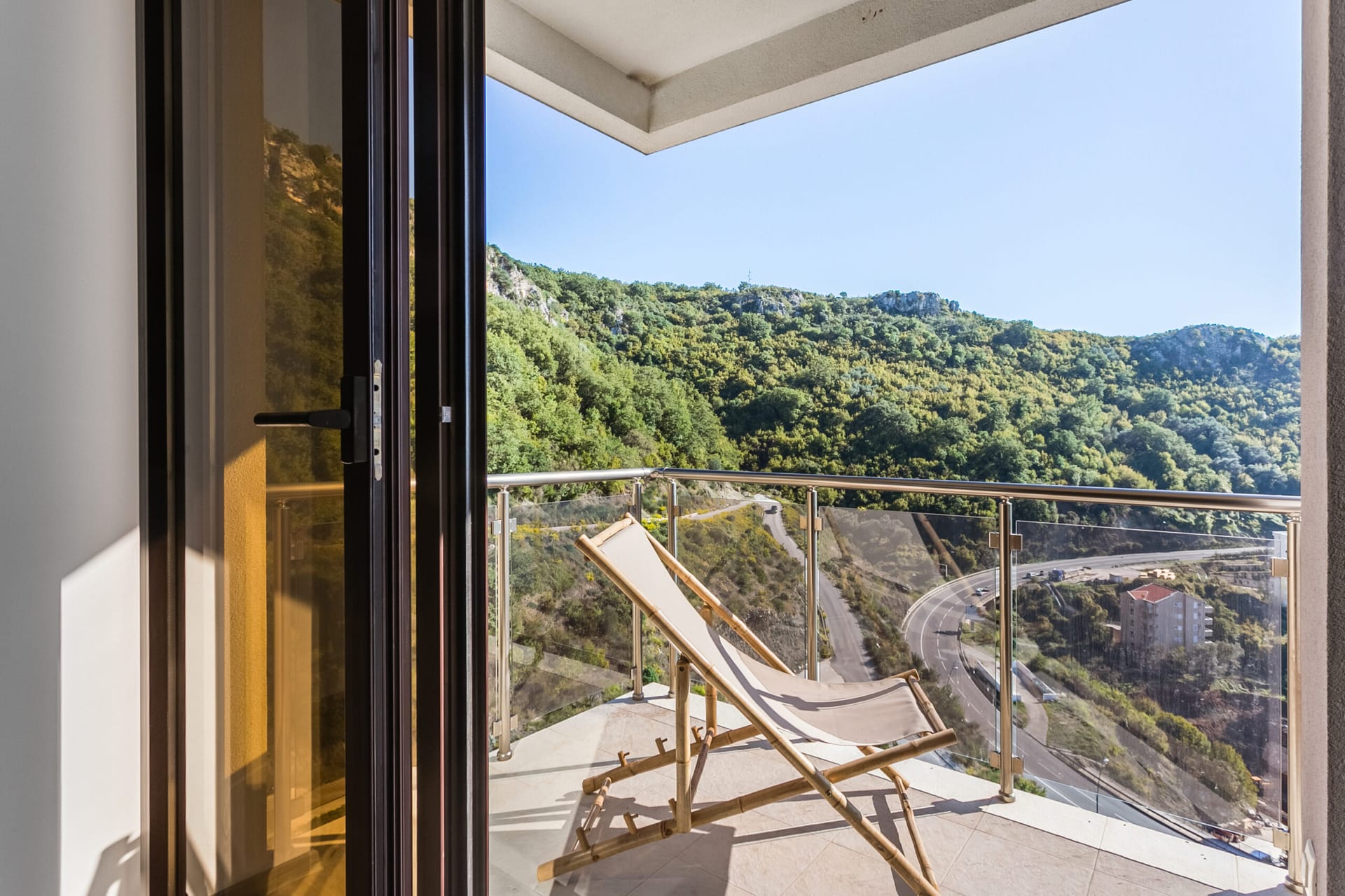 Balkon penthausa u Rafailovićima, Crna Gora: ležaljka, staklena ograda i panoramski pogled na planine i put.