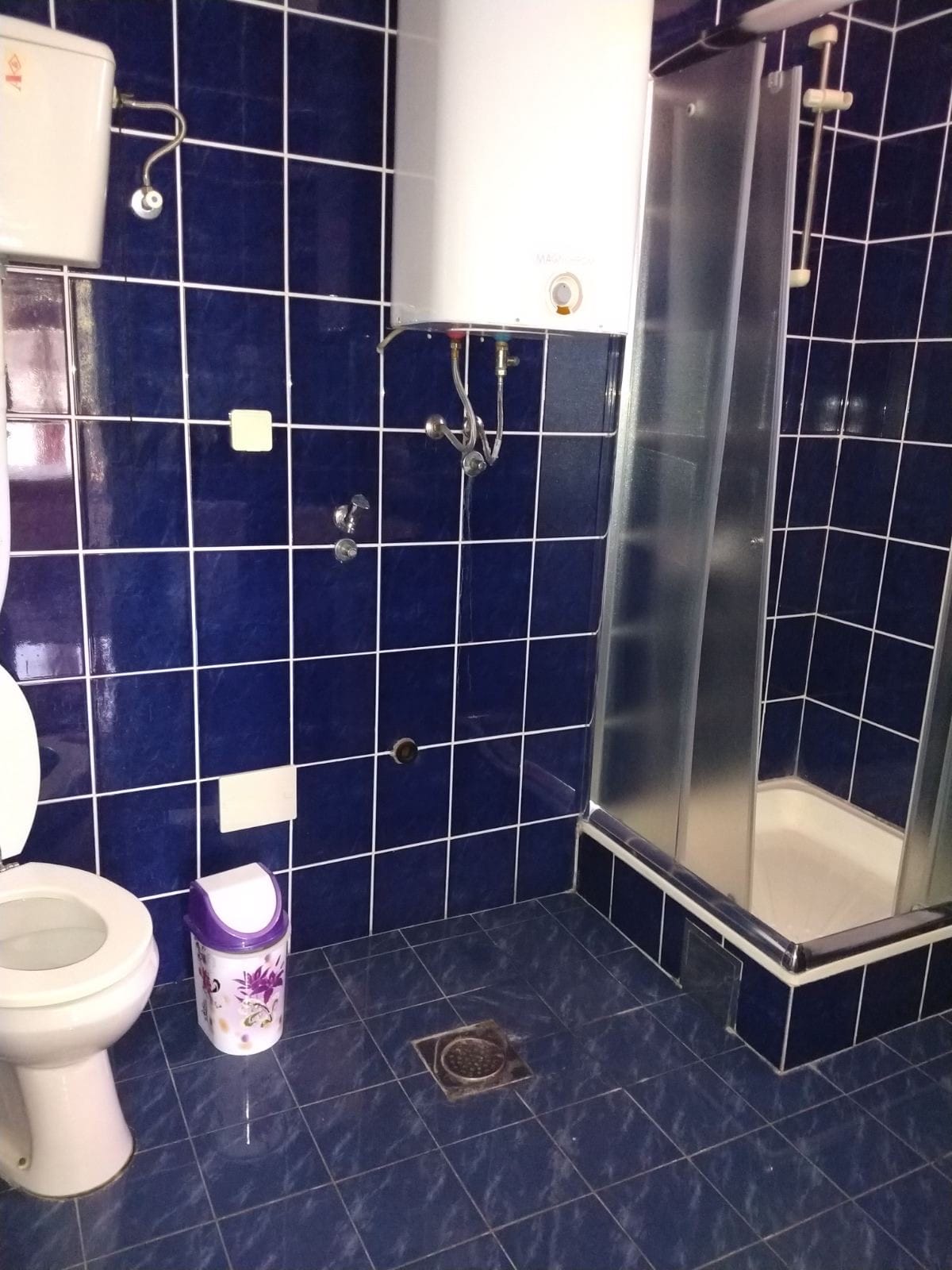 Salle de bain avec carrelage bleu, cabine de douche et chauffe-eau dans un mini-hôtel, Herceg Novi, Monténégro.