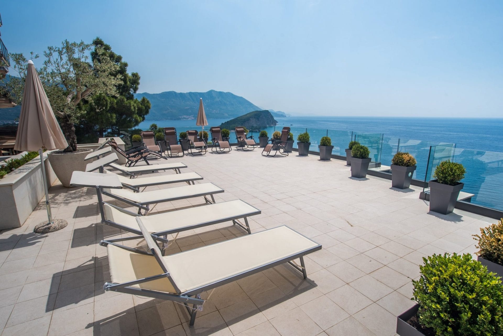 Terrace with loungers and panoramic views of the sea and island in Budva, Montenegro. Modern villa with a lounge area.