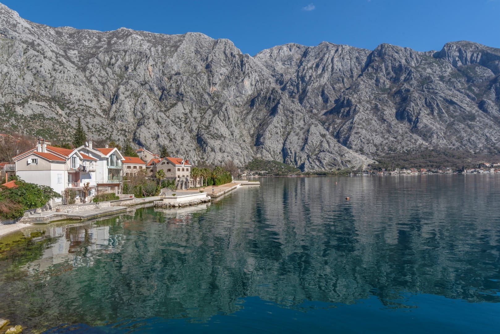 View of a residential complex by the sea in Orahovac, Bay of Kotor, Montenegro: houses with red roofs and mountains.