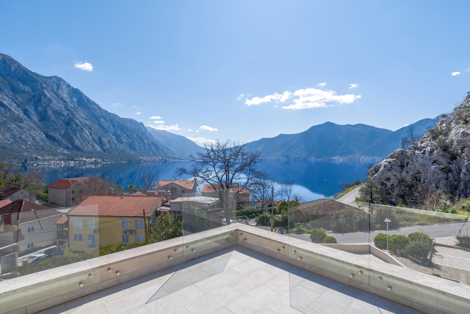 Panoramic view of the Bay of Kotor from the terrace of a residential complex in Orahovac, Montenegro, with glass railing.