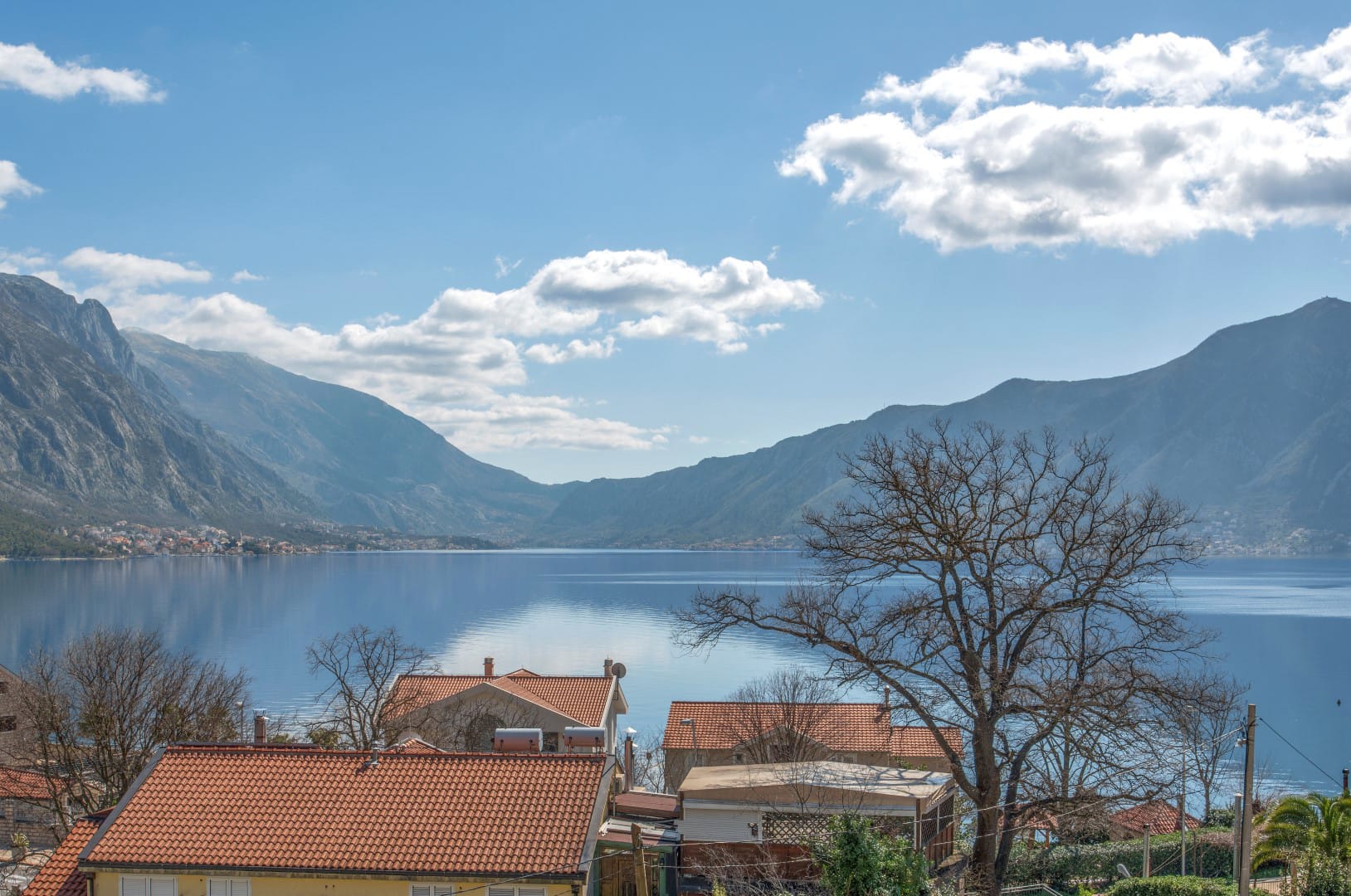 Panoramic view of the Bay of Kotor and mountains from a residential complex in Orahovac, Montenegro, with tiled roofs.