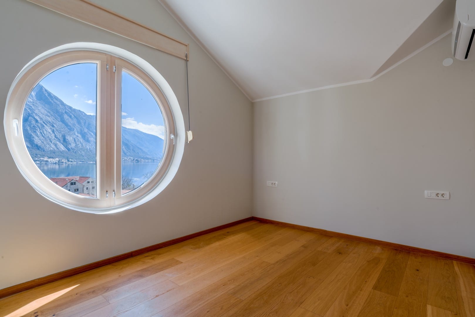 Bedroom with a round window and a view of the Bay of Kotor, Orahovac, Montenegro: light finishes and parquet flooring.