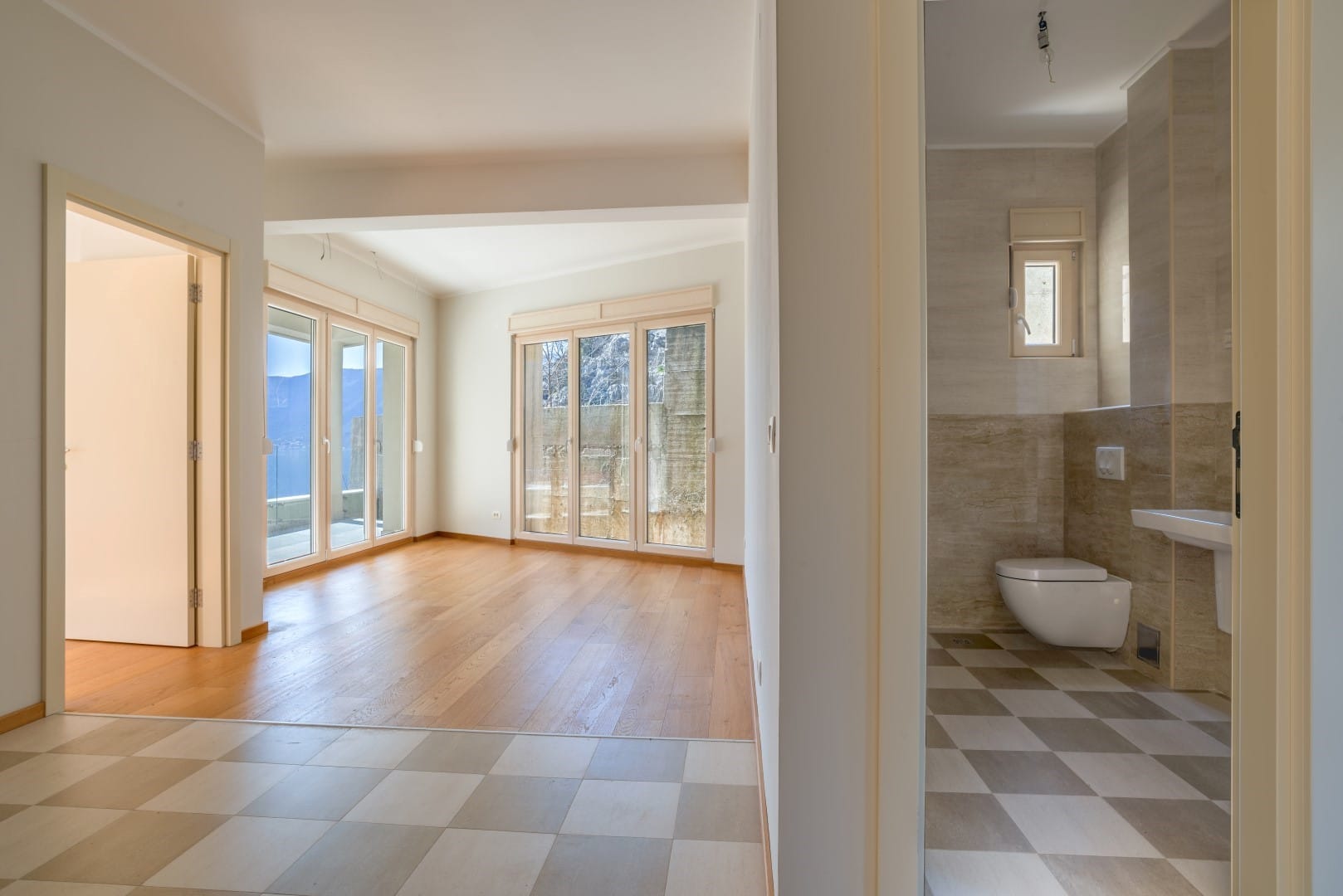 Bright living room with panoramic windows and sea view in the Orahovac residential complex, Montenegro, next to a modern bathroom.