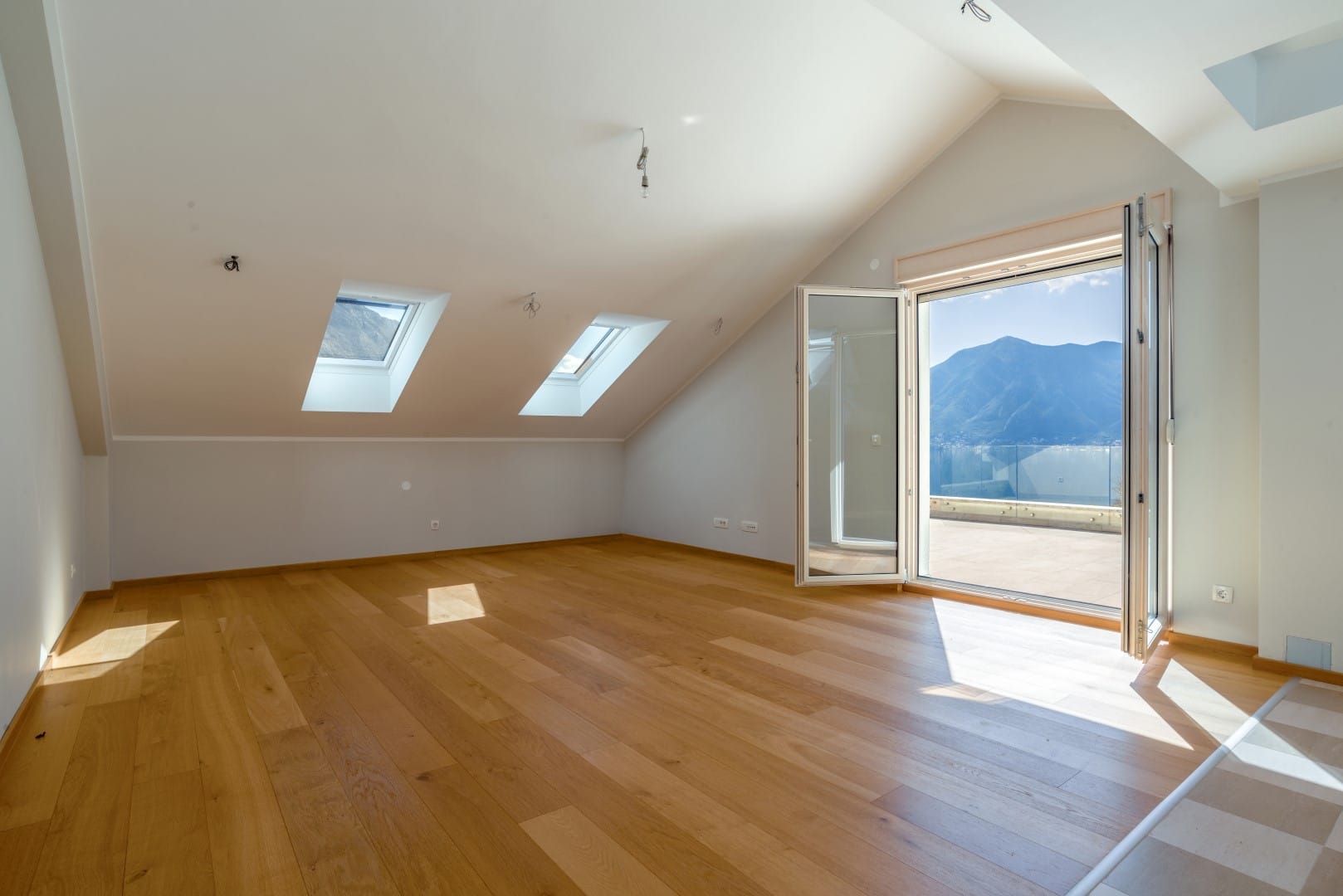 Bright attic living room with panoramic views of the mountains and sea in Orahovac, Montenegro, parquet flooring, and access to the terrace.