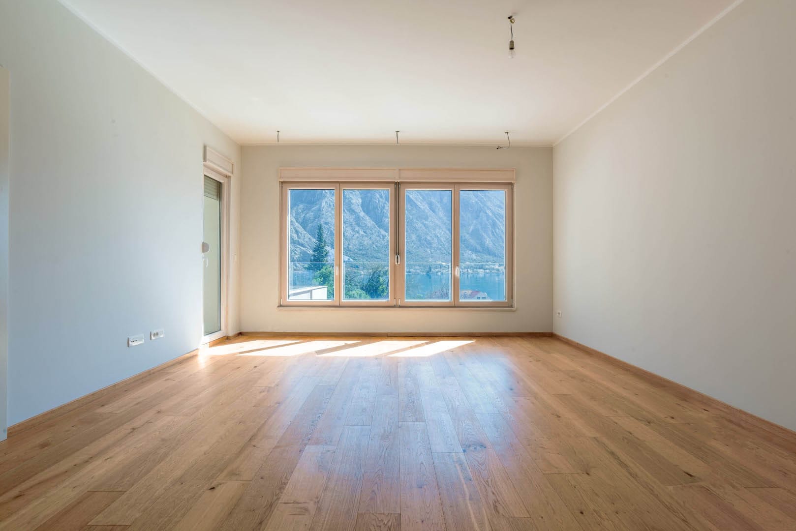 Bright living room with parquet flooring and panoramic views of the Bay of Kotor in the Orahovac residential complex, Montenegro.