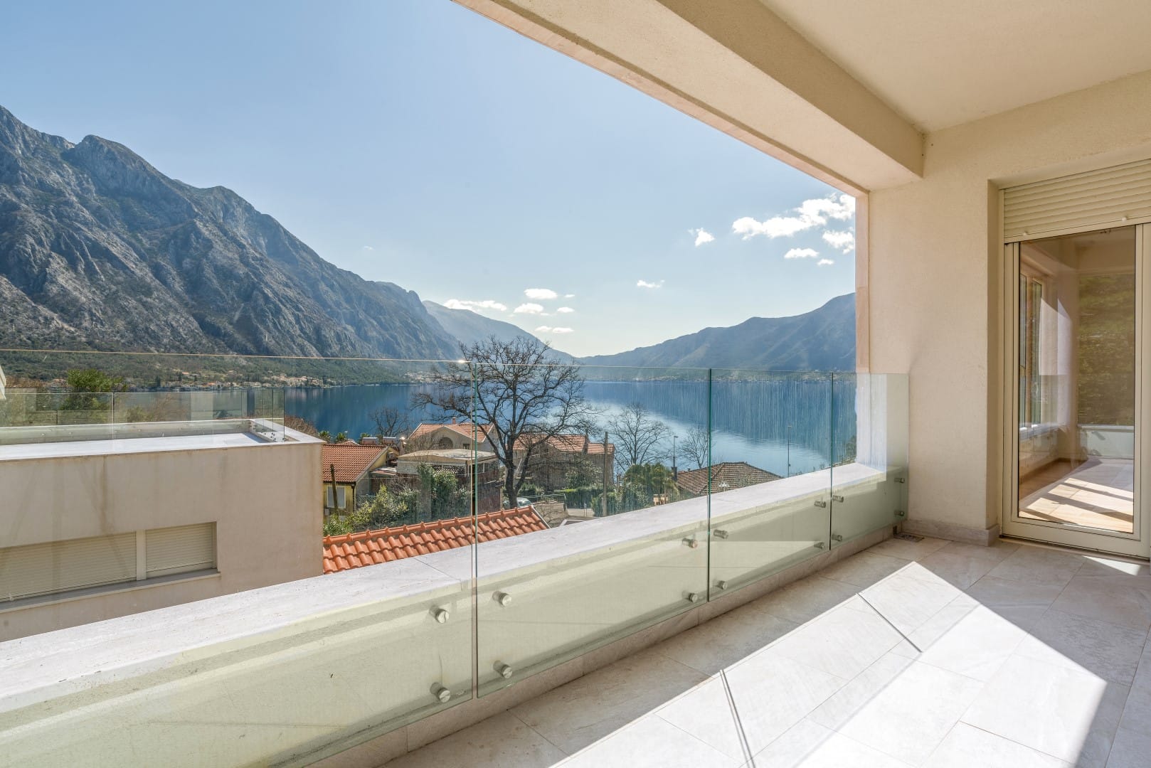 Terrace with panoramic views of the Bay of Kotor and mountains in the Orahovac residential complex, Montenegro: glass railing and tile.
