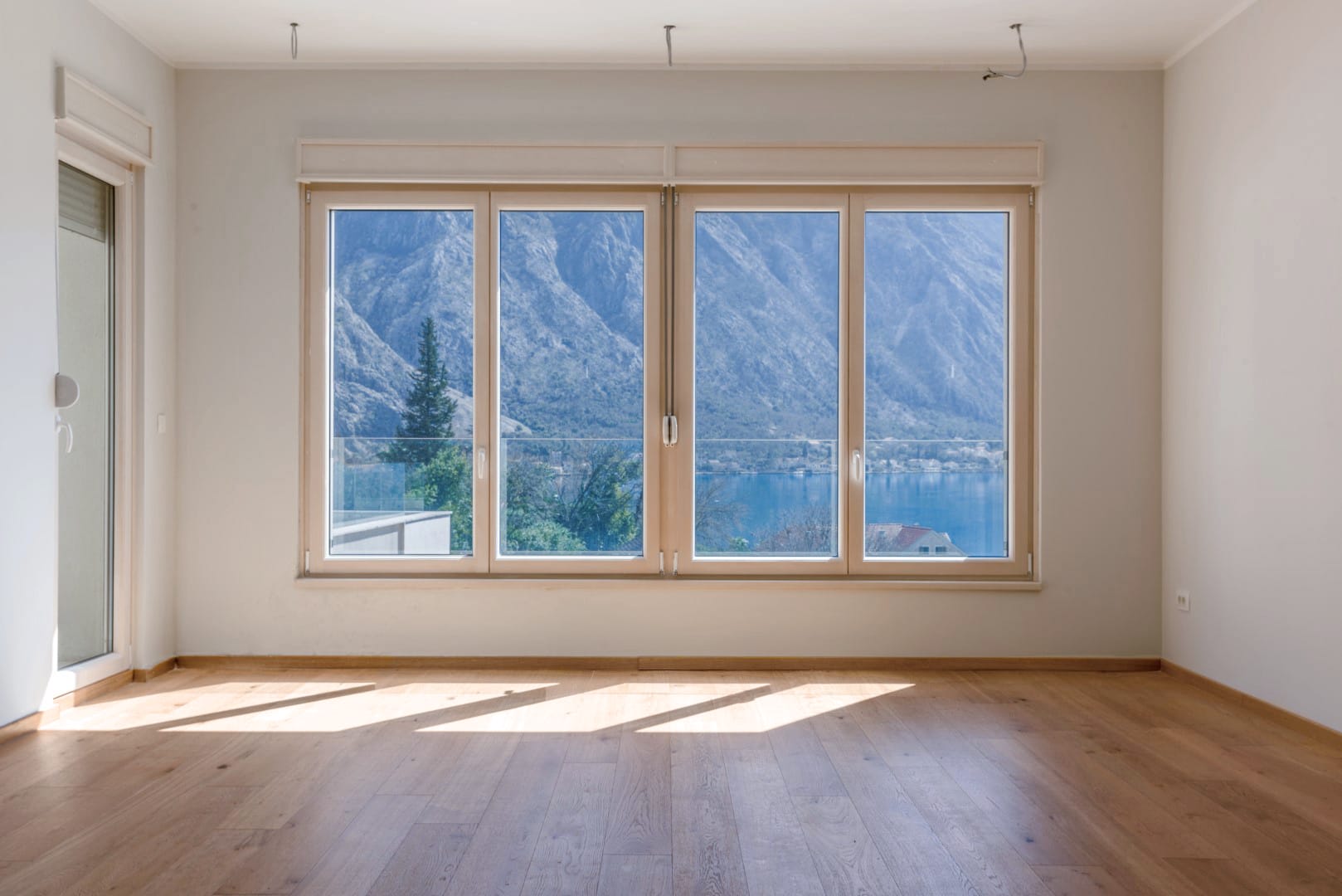 Bright living room with panoramic views of the mountains and sea in Orahovac, Montenegro, wooden floor and large windows.