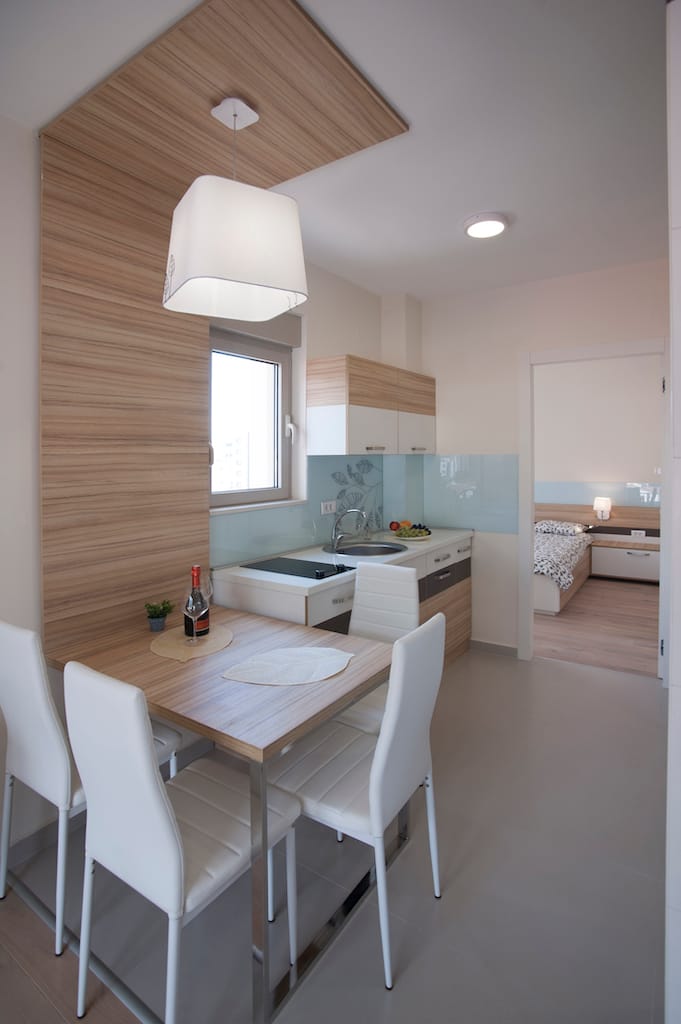 Savremena kuhinja-trpezarija u apartmanima Budve, Crna Gora: svetao nameštaj, trpezarijski deo i pogled na spavaću sobu.
