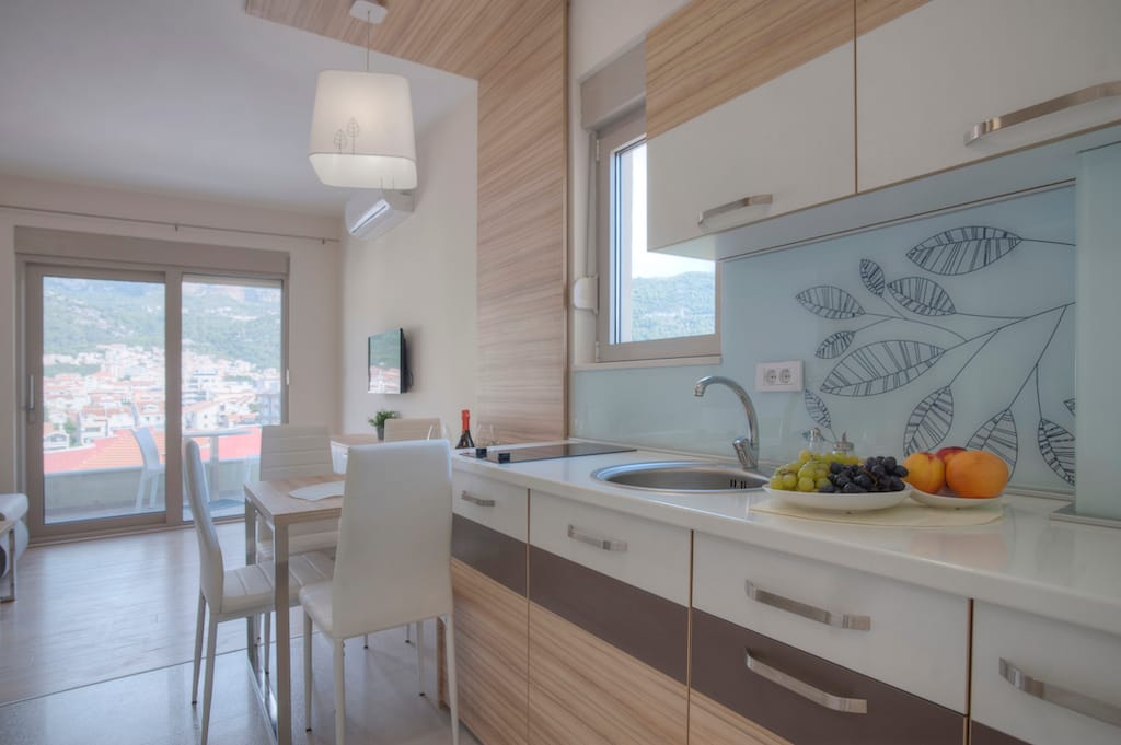 Savremena kuhinja u apartmanima Budve, Crna Gora: svetao kuhinjski nameštaj, trpezarijski deo i izlaz na terasu s pogledom.