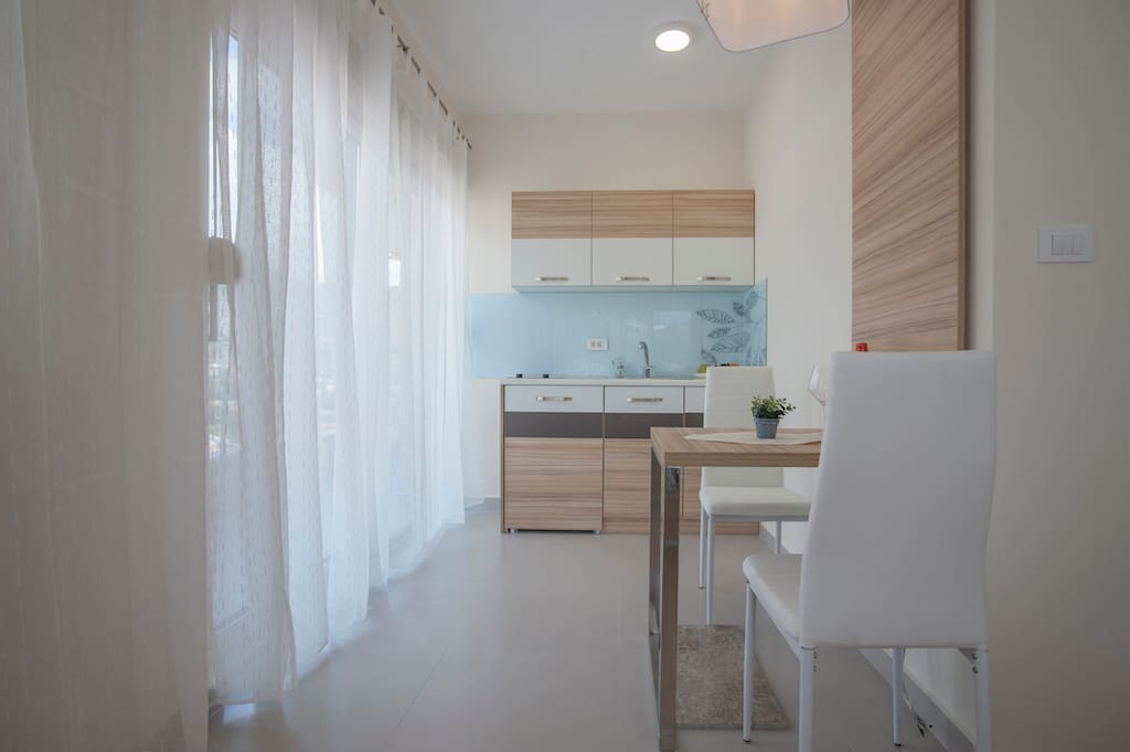 Savremena kuhinja-trpezarija u apartmanima Budve, Crna Gora: svetao nameštaj, trpezarijski deo i panoramski prozor.