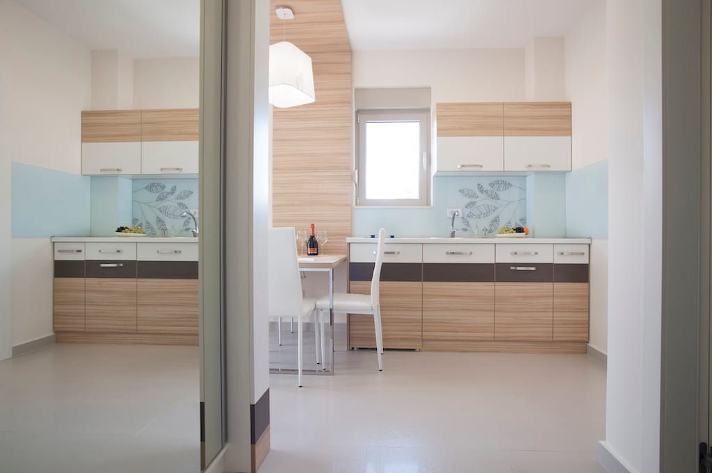 Savremena kuhinja u apartmanima u Budvi, Crna Gora: svetao kuhinjski nameštaj, trpezarijski deo i stilizovana obrada zidova.