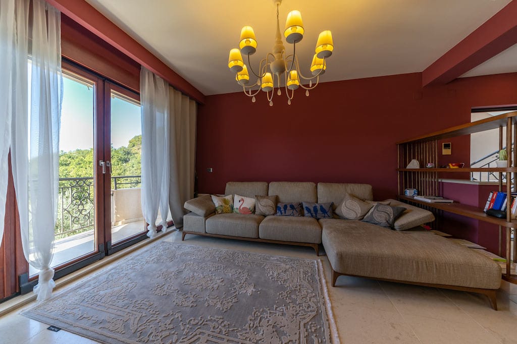 Living room in an apartment in Petrovac, Montenegro: beige corner sofa, vintage chandelier, and access to a balcony with a view.