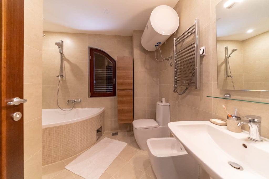 Modern bathroom in an apartment in Petrovac, Montenegro: corner bathtub, bidet, shower, and light-colored tiles.