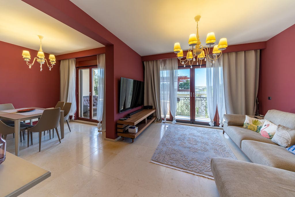 Living room with dining area in an apartment in Petrovac, Montenegro: light furniture, terracotta walls, and access to the terrace.