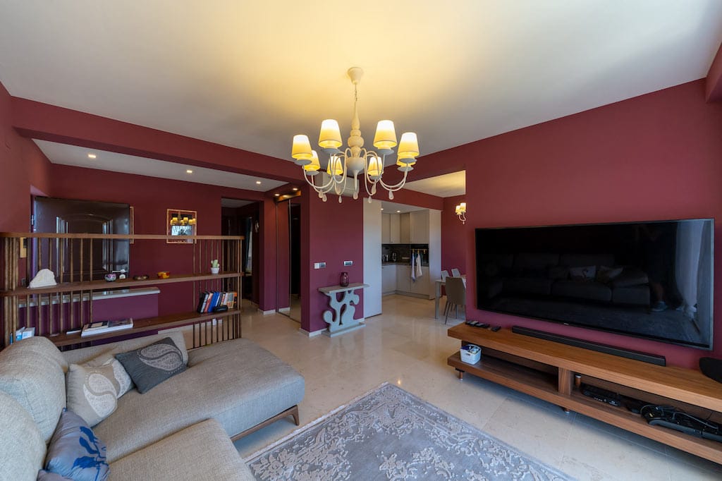 Living room in an apartment in Petrovac, Montenegro: burgundy walls, a light sofa, TV area, and a dining area with kitchen.