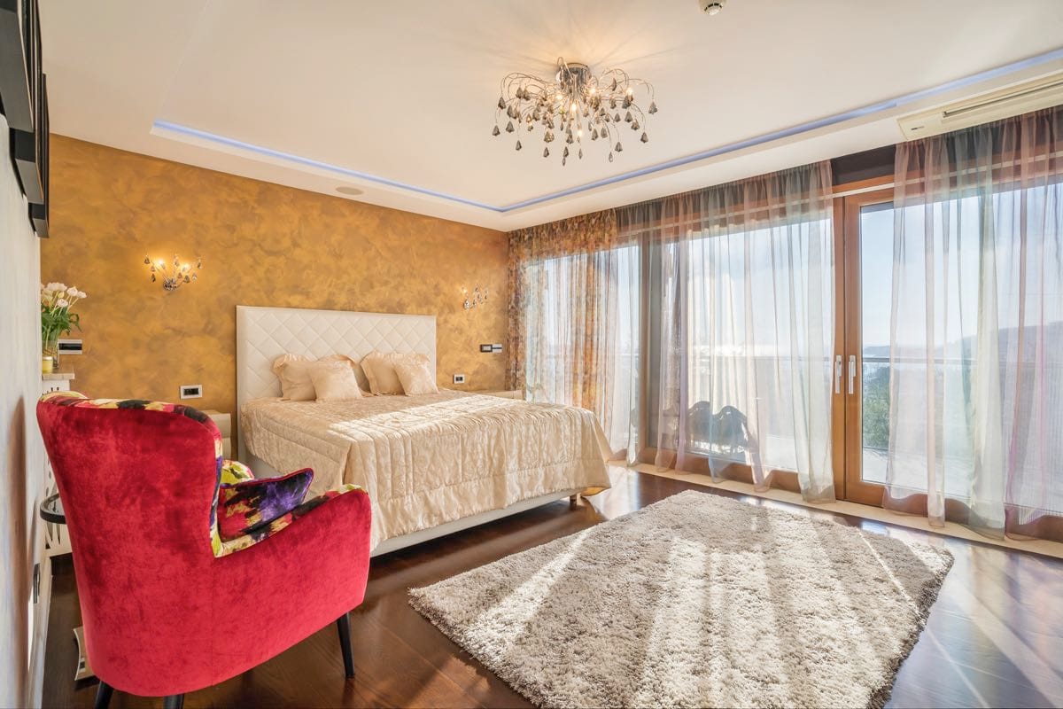 Spavaća soba sa bračnim krevetom, crvenom foteljom i panoramskim prozorima u vili u Budvi, Crna Gora.