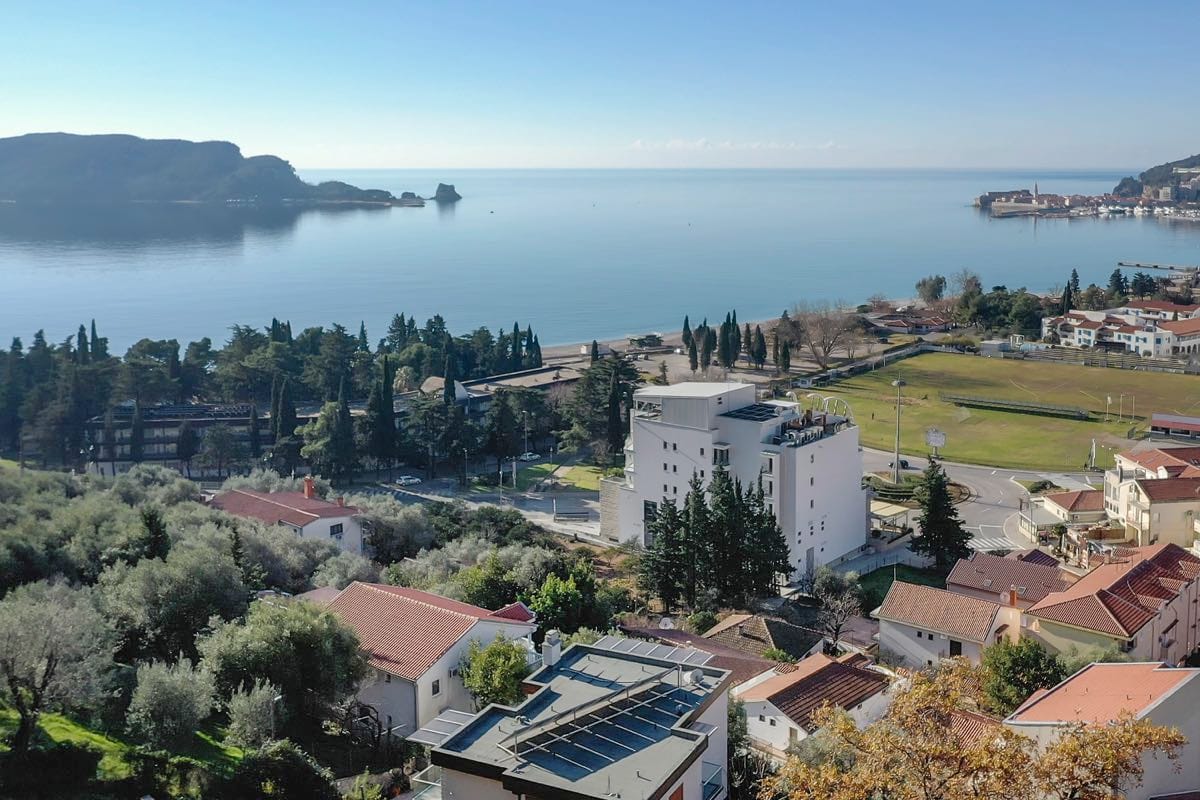 Panoramski pogled na more i obalu Budve, Crna Gora: moderna vila, maslinjaci i plaža u daljini.