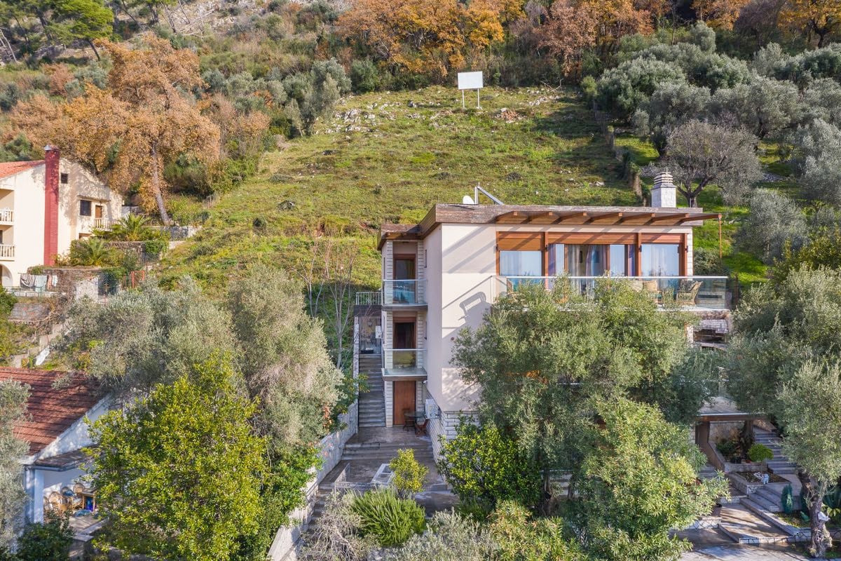 Trospratna vila u Budvi, Crna Gora, sa terasama, panoramskim prozorima i zelenim vrtom na padini planine.