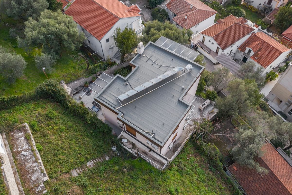 Pogled iz vazduha na vilu u Budvi, Crna Gora: ravni krov sa solarnim panelima, terasa i zelena parcela oko nje.