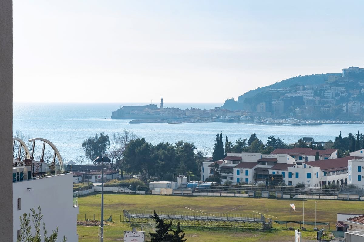 Pogled sa balkona vile u Budvi, Crna Gora: panorama Jadranskog mora, starog grada i fudbalskog terena.