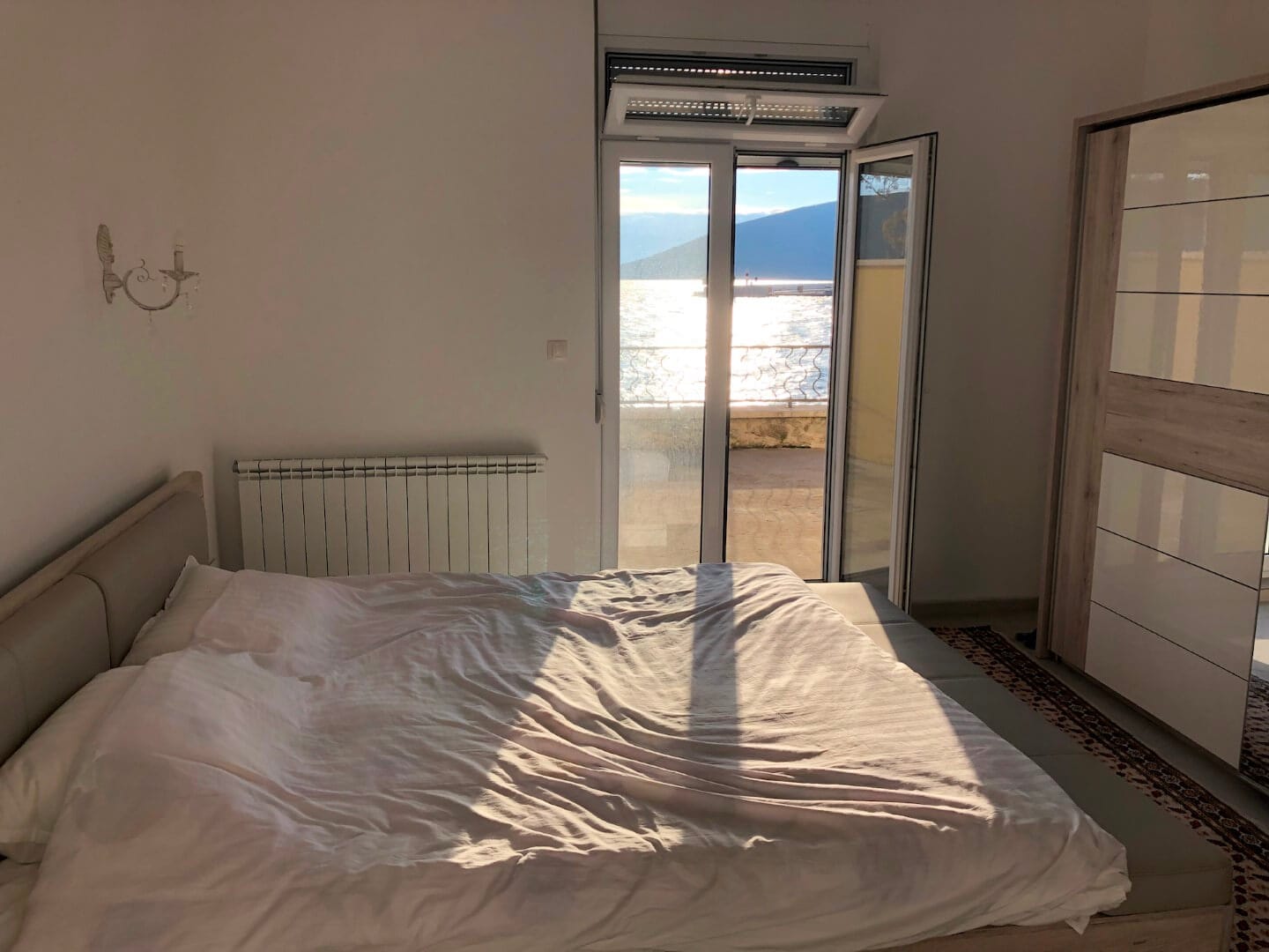 Schlafzimmer in einer Wohnung in Herceg Novi, Montenegro: Doppelbett, Kleiderschrank und Zugang zur Terrasse mit Blick auf das Meer und die Berge.