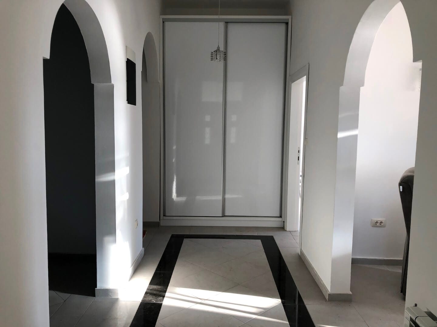 Heller Flur mit weißen Bögen und Einbauschrank in einer Wohnung, Herceg Novi, Montenegro. Boden mit schwarzer Umrandung.