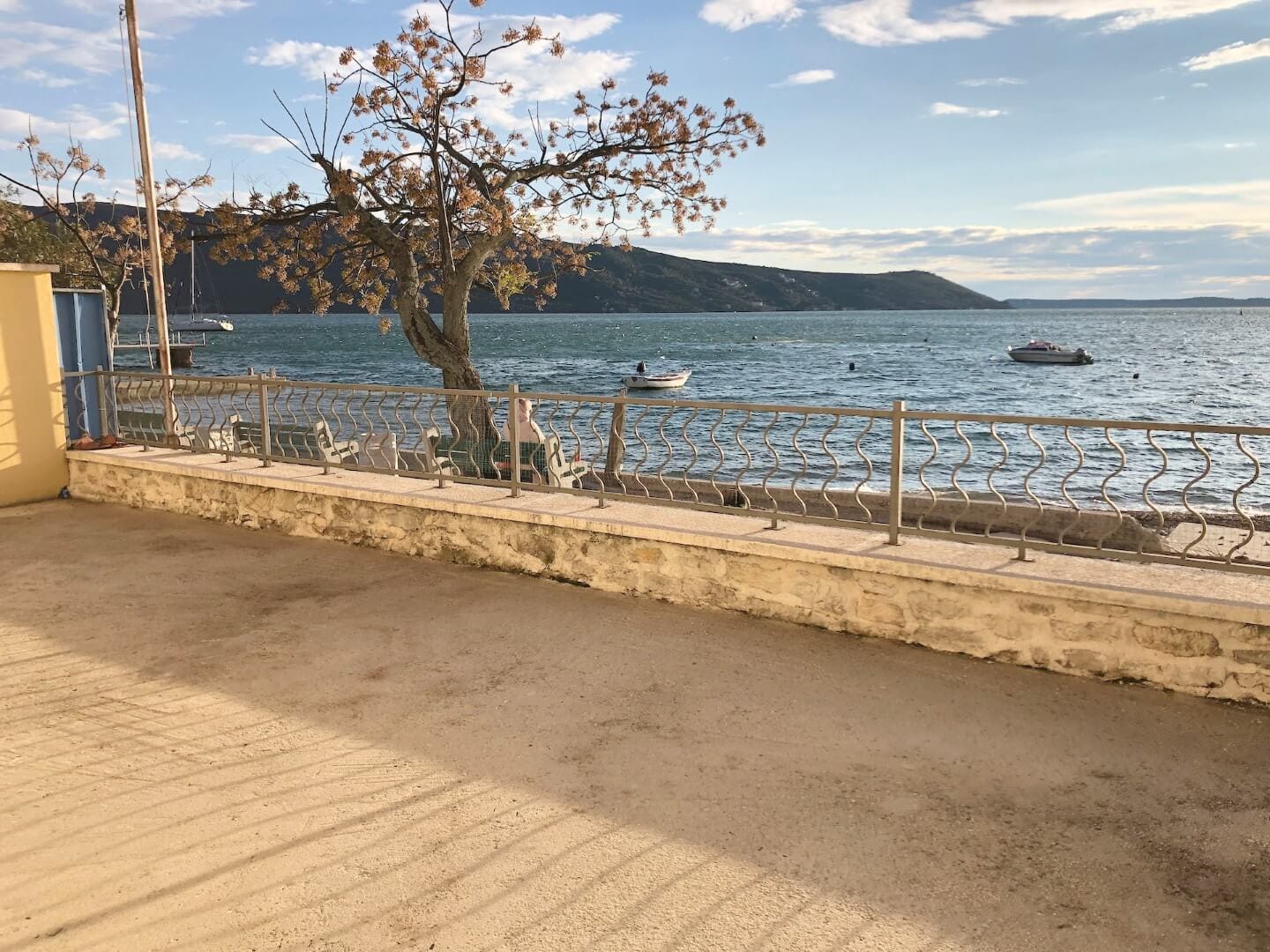 Blick auf das Meer und die Bucht von Kotor von der Terrasse der Wohnung in Herceg Novi, Montenegro: Uferpromenade, Baum und Boote.