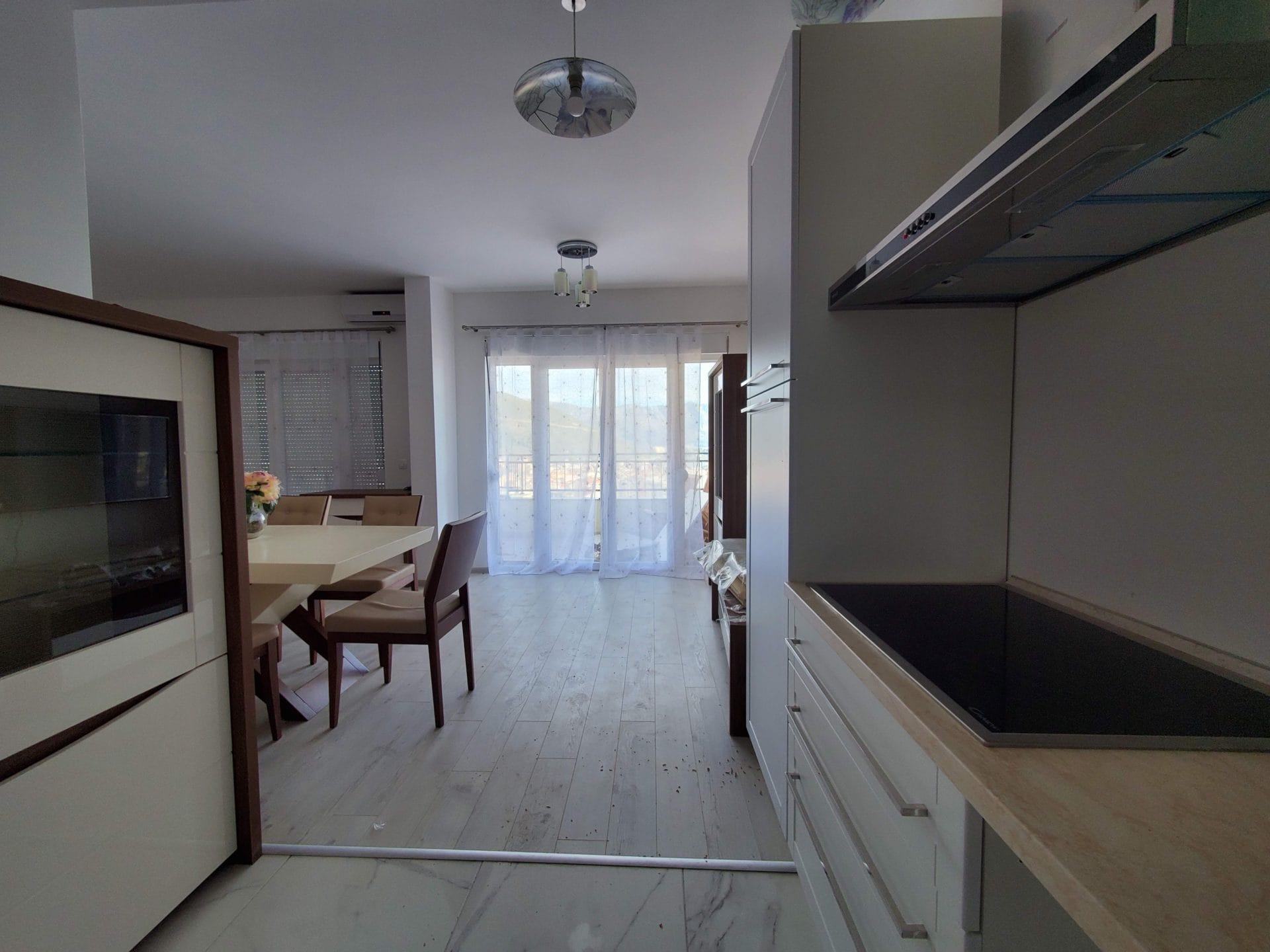 Savremena kuhinja-dnevna soba u stanu u Budvi, Crna Gora: svetao nameštaj, trpezarijski deo i izlaz na balkon.
