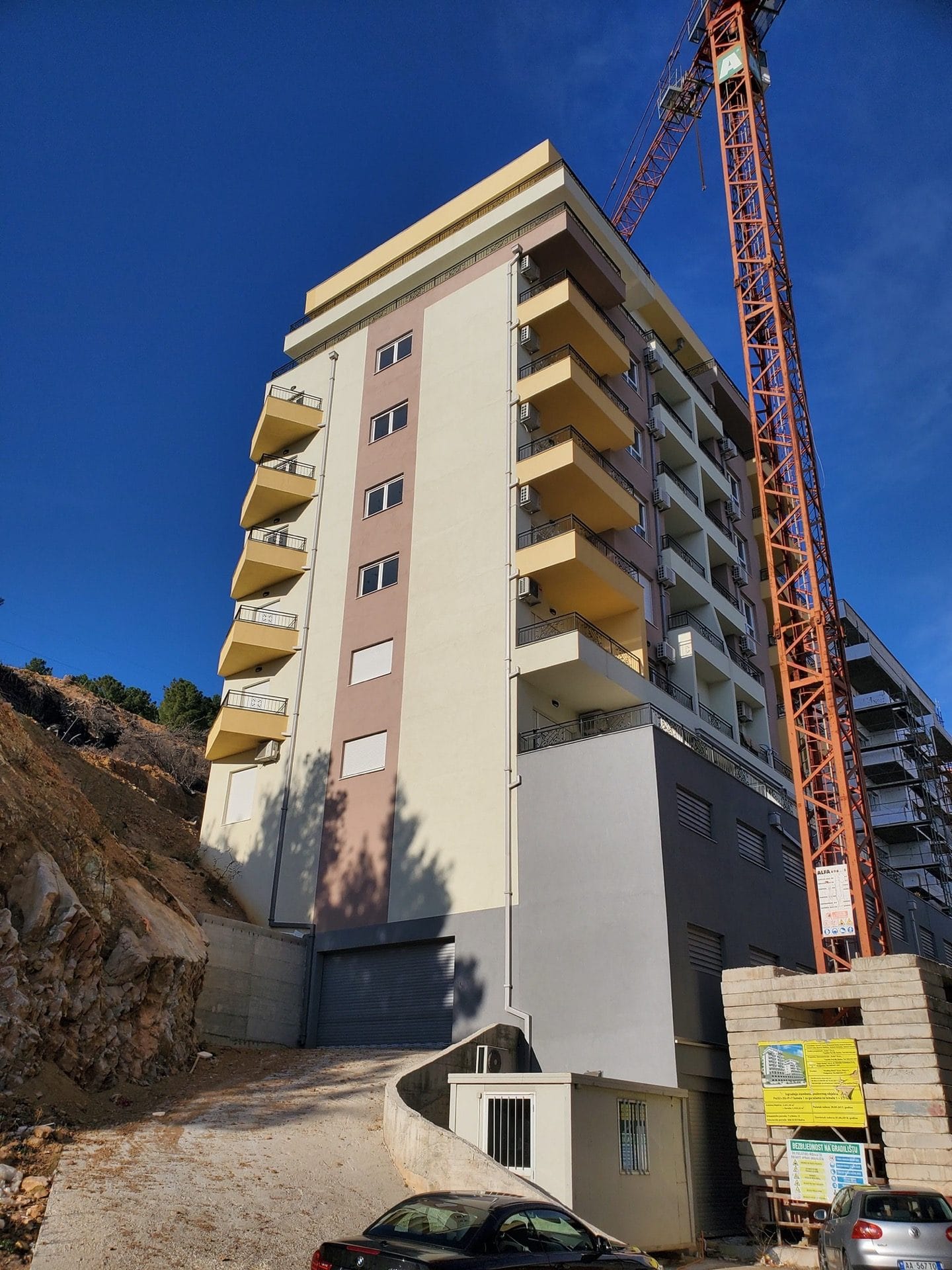 An apartment complex under construction in Budva, Montenegro: a modern building with balconies and a construction crane.