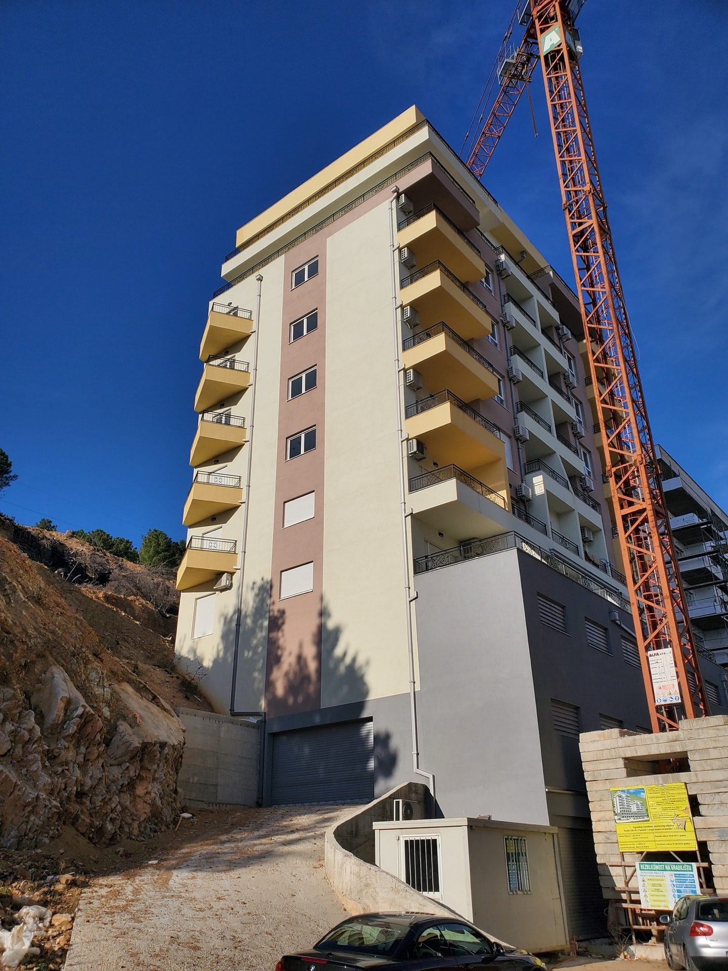An apartment building under construction with balconies in Budva, Montenegro: view of the facade and a construction crane.
