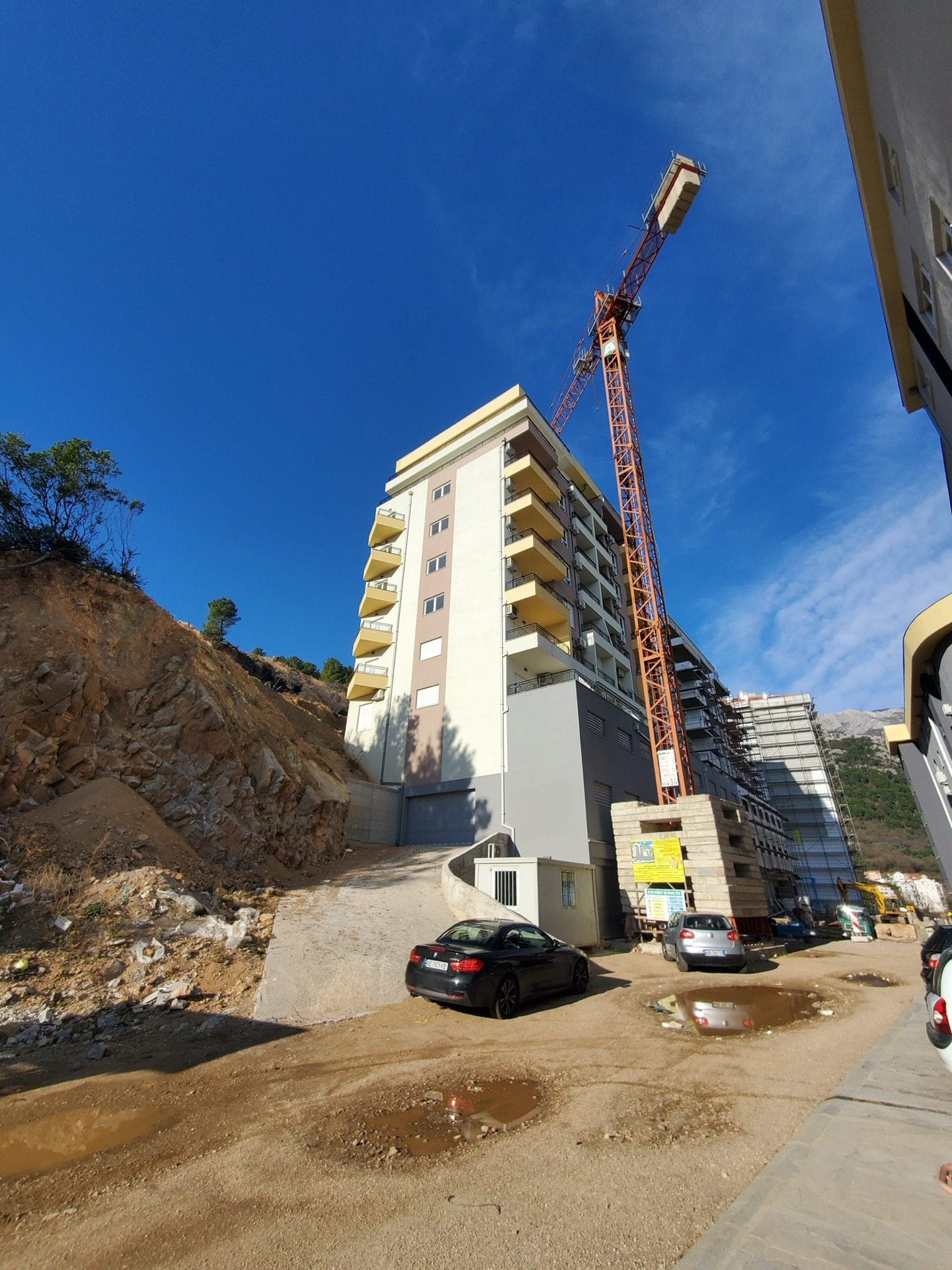Residential complex under construction in Budva, Montenegro: a multi-story building with balconies, a construction crane, and the surrounding area