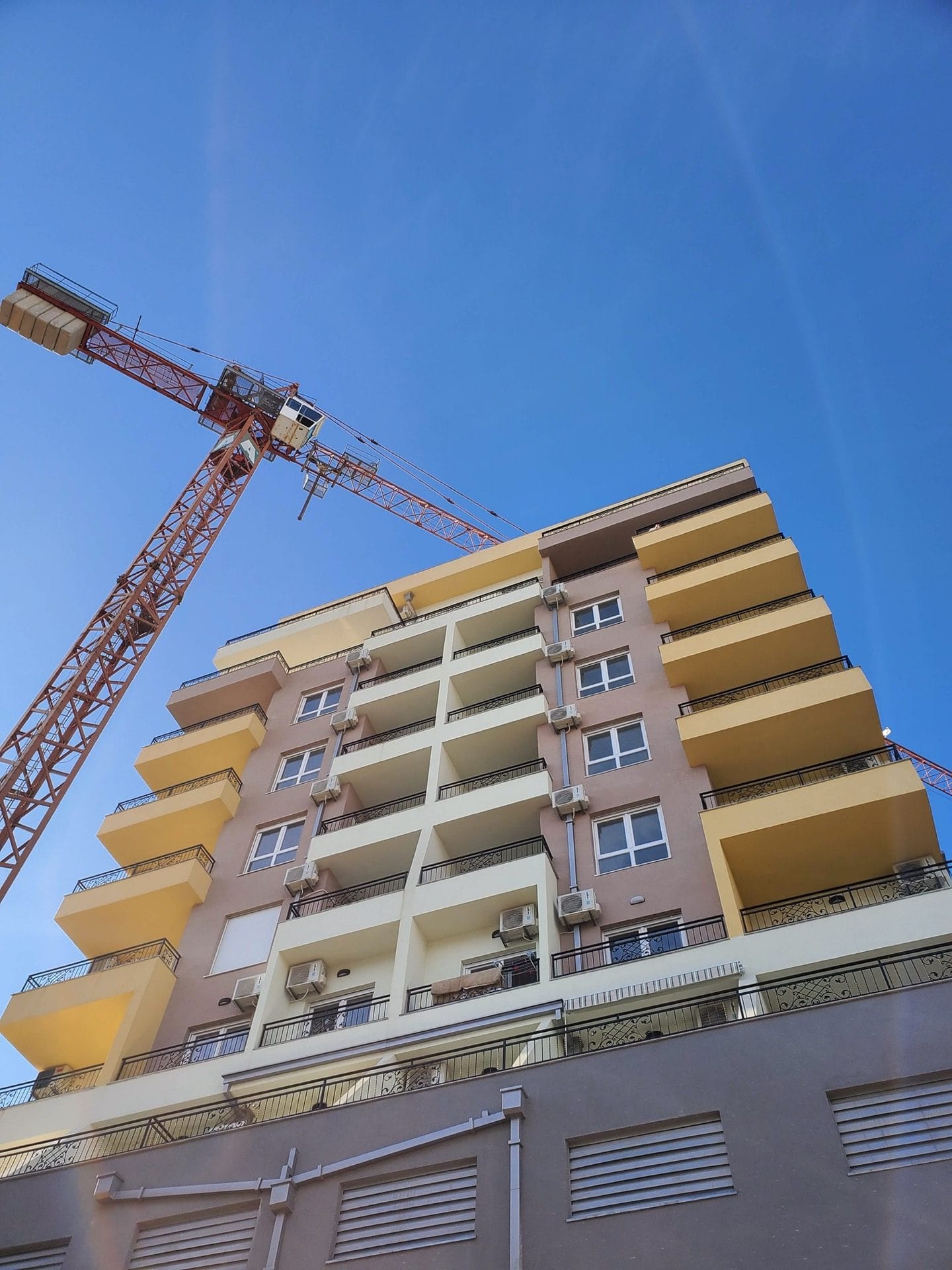 Residential complex under construction in Budva, Montenegro: a modern building with balconies and a construction crane against the sky.