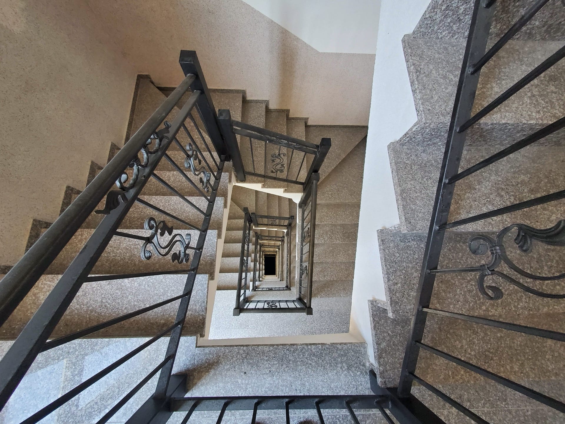 Spiral staircase with wrought-iron railings and stone steps in a residential complex, Budva, Montenegro.