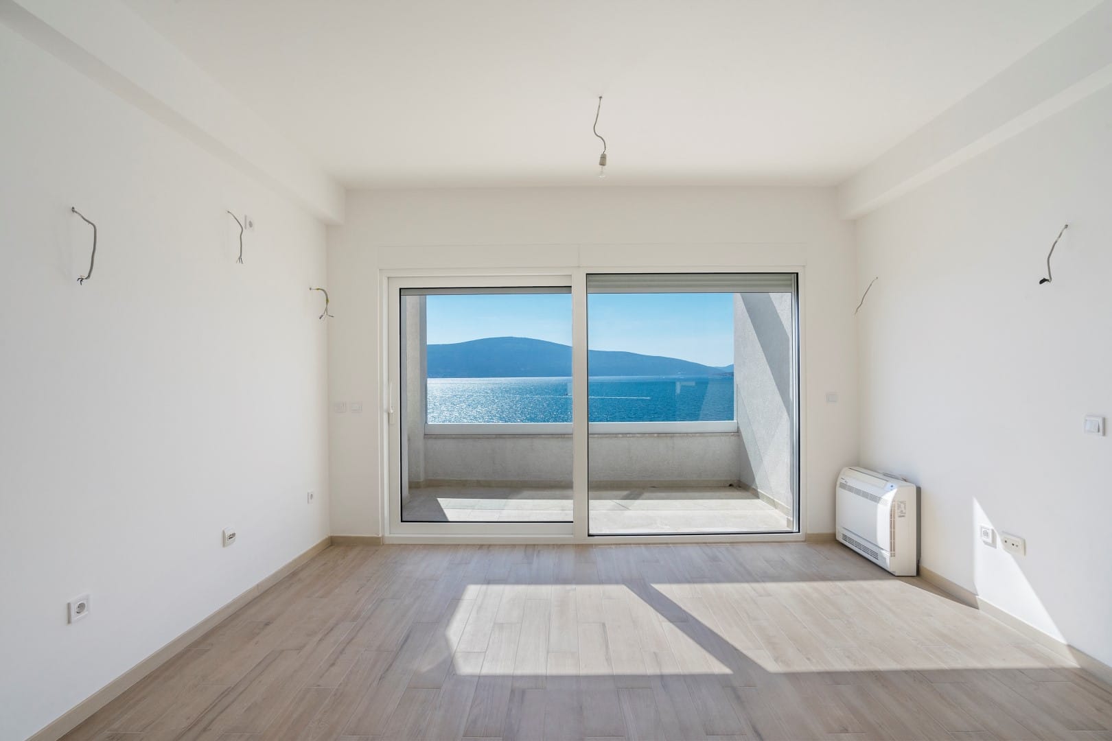 Svetao dnevni boravak u novogradnji u Tivtu, Crna Gora, sa panoramskim pogledom na more i izlazom na balkon.