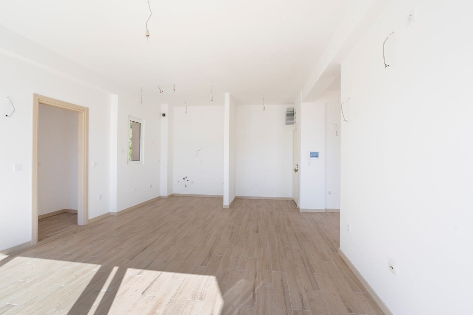 Svetla dnevna soba bez nameštaja u novogradnji, Tivat, Crna Gora: beli zidovi, podne pločice u imitaciji drveta, renovirano.