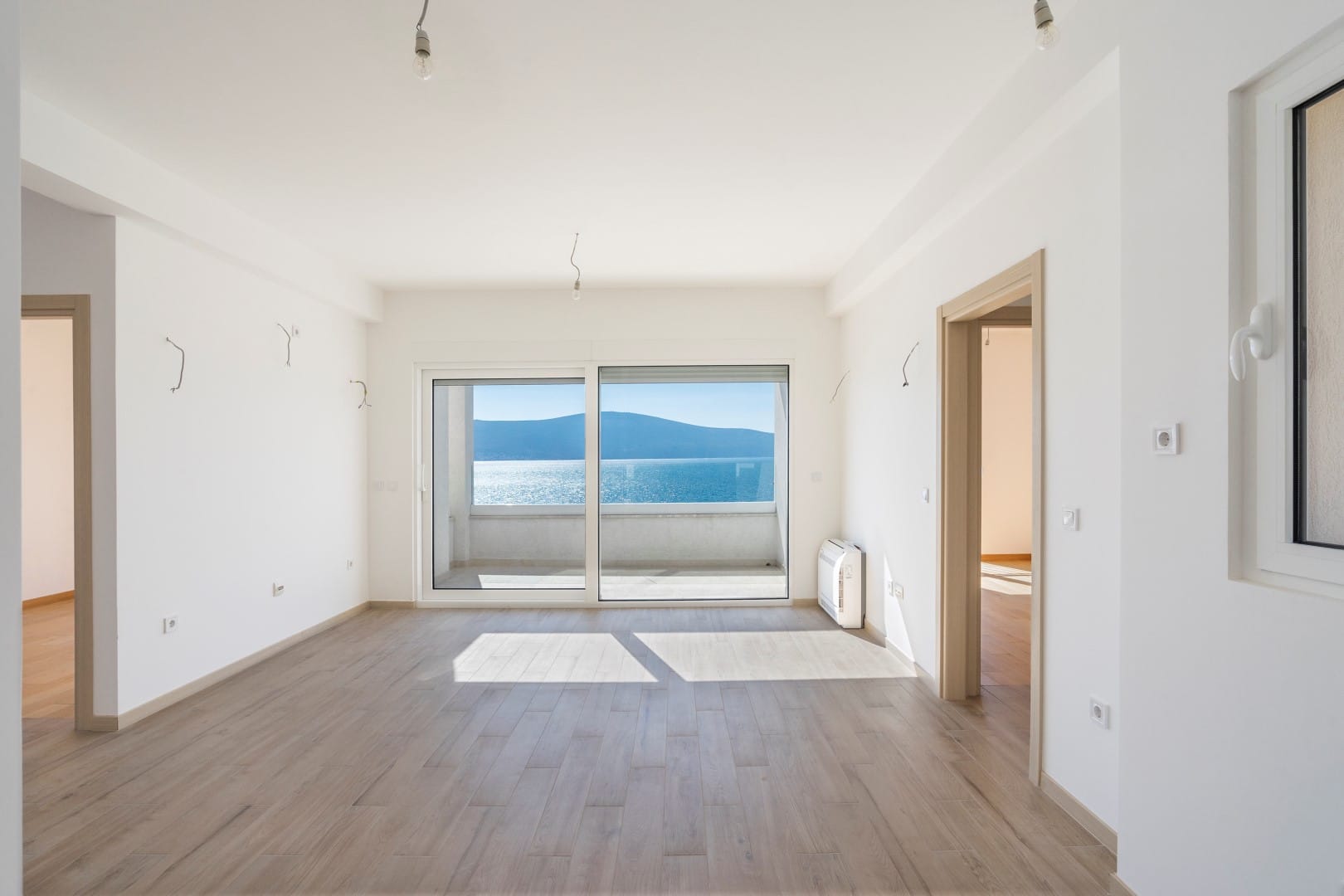 Svetao dnevni boravak u novom stanu u Tivtu, Crna Gora, sa panoramskim pogledom na more i izlazom na terasu.