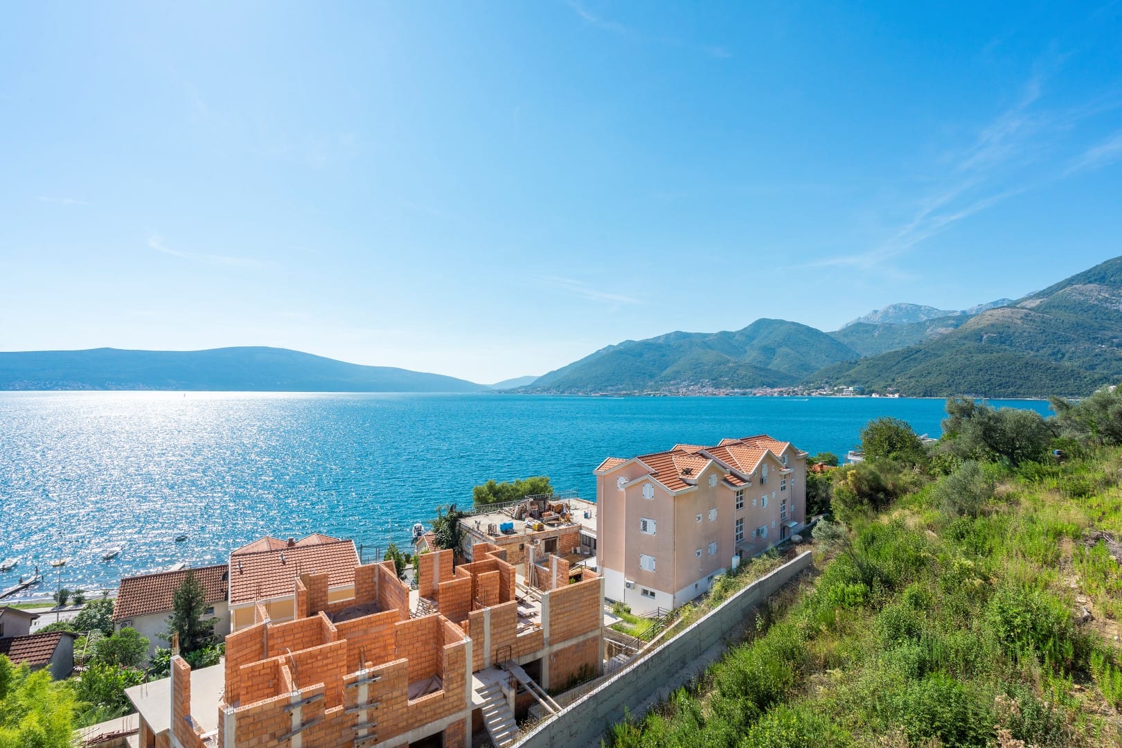 Stambeni kompleks u izgradnji u Tivtu, Crna Gora, sa panoramskim pogledom na more i planine po sunčanom danu.
