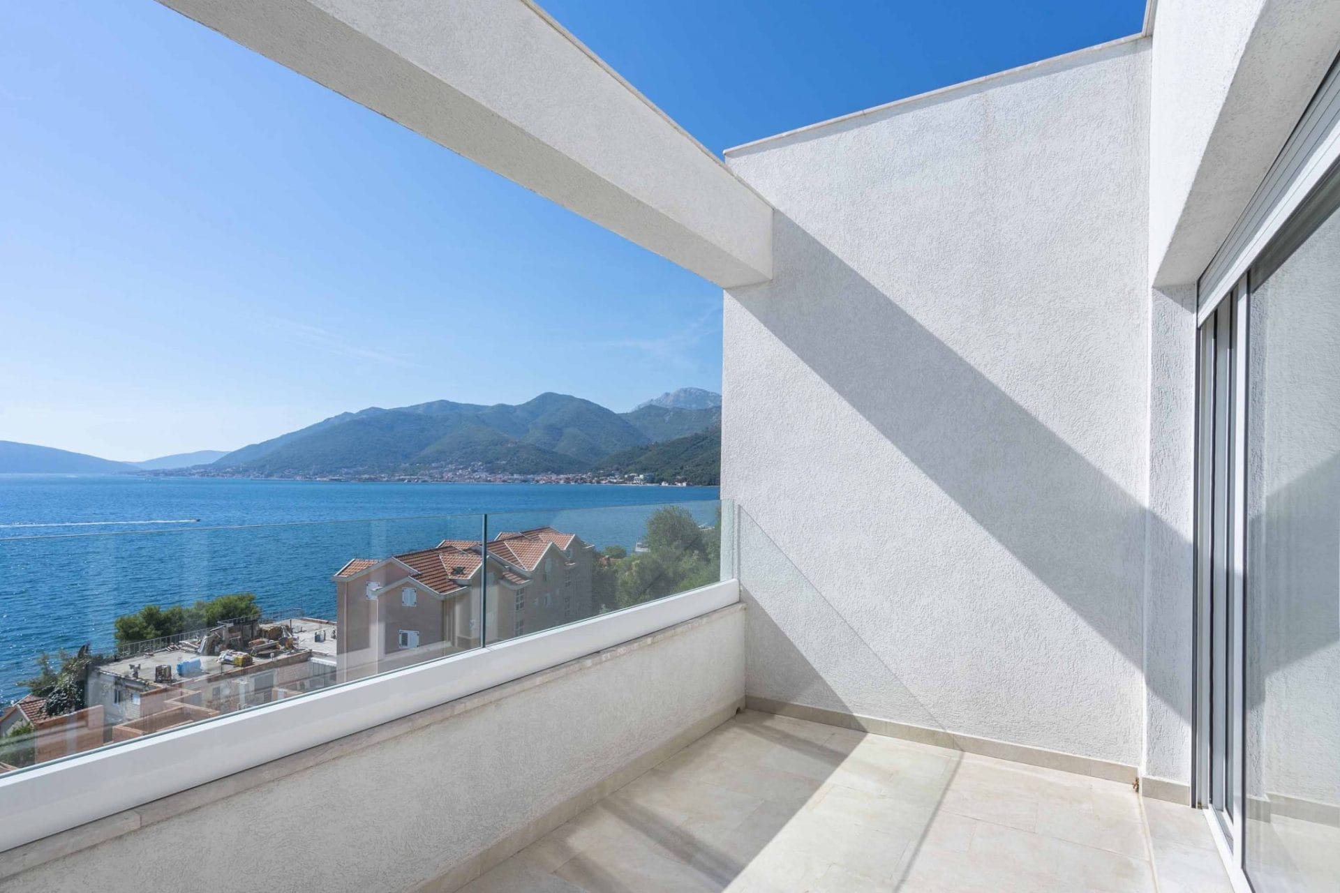 Moderan balkon sa panoramskim pogledom na more i planine u stanu, Tivat, Crna Gora. Staklena ograda, svetla završna obrada.
