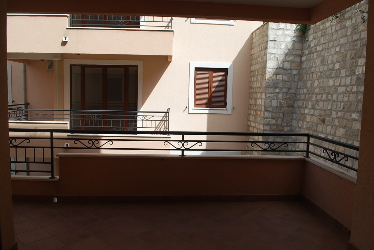 Prostran balkon sa kovanim ogradama u stanu, Risan, Crna Gora: pogled na fasadu zgrade i kameni zid.