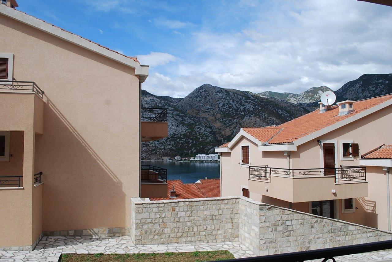 Pogled na Bokokotorski zaliv i planine iz apartmana u Risnu, Crna Gora: moderne kuće sa krovovima od crepa i terasama.