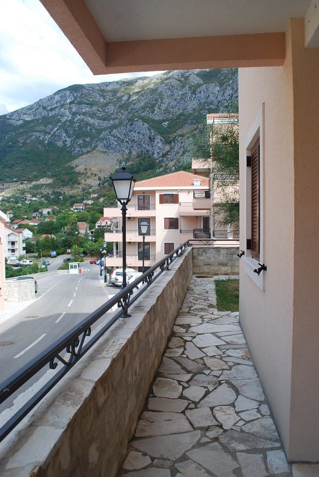 Prostran balkon sa kamenim oblogama i pogledom na planine i grad Risan, Crna Gora, u stambenom kompleksu sa kovanom ogradom.