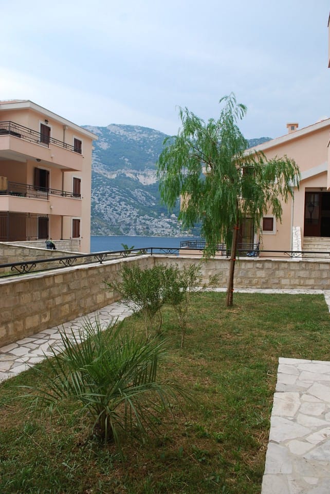 Pogled na stambeni kompleks u Risnu, Crna Gora: uređena bašta sa drvećem i panoramski pogled na more i planine.