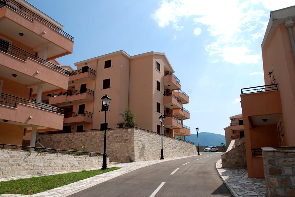 Savremeni stambeni kompleks sa terasama u Risnu, Crna Gora: pogled na niske zgrade sa kamenim oblogama i put.