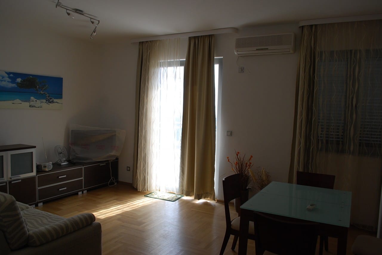 Svetla dnevna soba sa nameštajem, parketom i izlazom na balkon u stanu u Budvi, Crna Gora. Moderan enterijer.